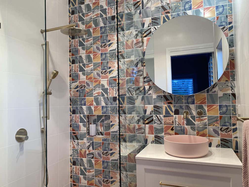 A vibrant, modern bathroom featuring a full-height accent wall of artistic square tiles with abstract brushstroke patterns in blue, peach, and grey.