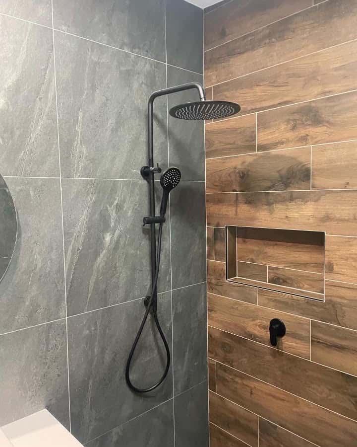 A close-up view of a modern shower corner featuring a combination of large, dark grey stone-look tiles and horizontal wood-look plank tiles.