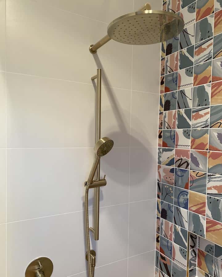 A close-up view of a modern shower featuring brushed gold fixtures, including a large rainfall showerhead and a sliding handheld wand.