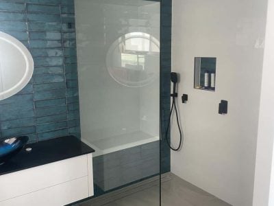 A modern, high-contrast bathroom featuring a walk-in shower with matte black fixtures, including a ceiling-mounted square rainfall showerhead and a handheld wand.